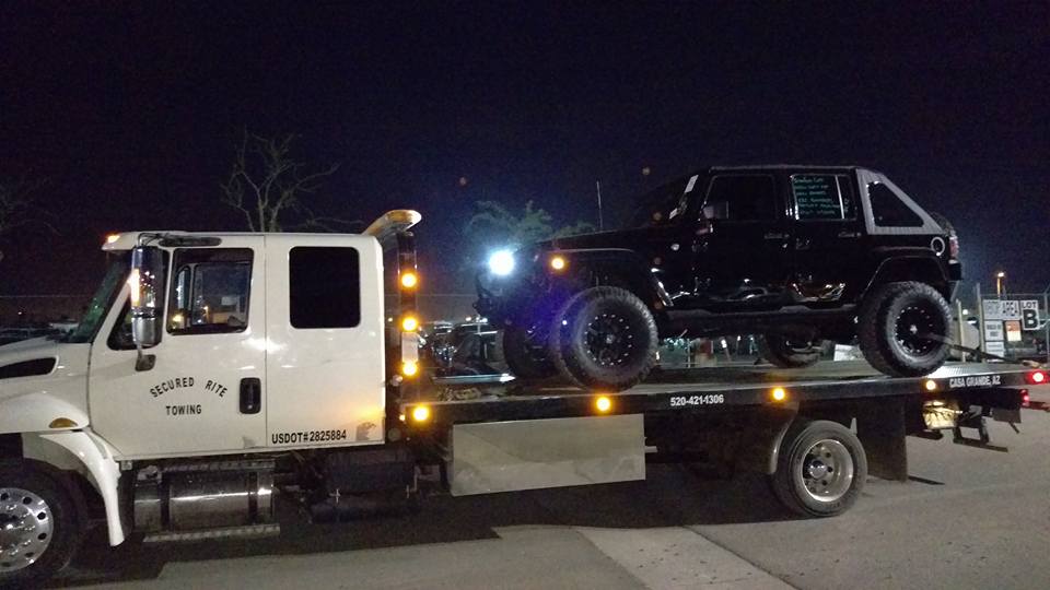 Secured Rite Towing flatbed carrying a lifted vehicle at night